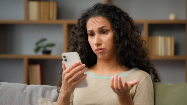 istock Hispanic sad displeased woman has problem with online mobile app on cell phone unhappy with blocked account in social networks looking at cellphone screen scam unsuccessful bad news sitting at home 2190436515