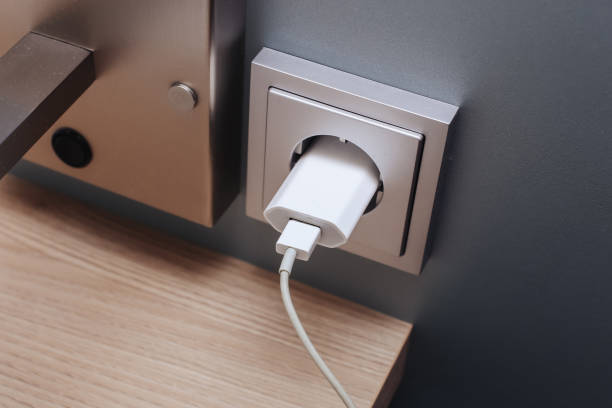 Phone charger with cable plugged into a wall socket. Hotel bedside shelf with charging setup.