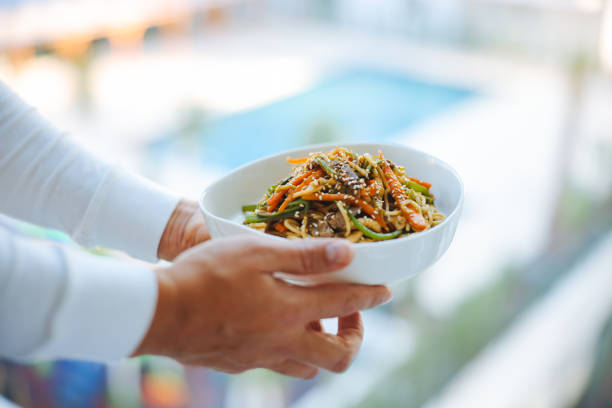 Stir-fry with soba noodles, meat and vegetables in white plate on a light background. Asian fast and healthy food concept. Top view and copy space.