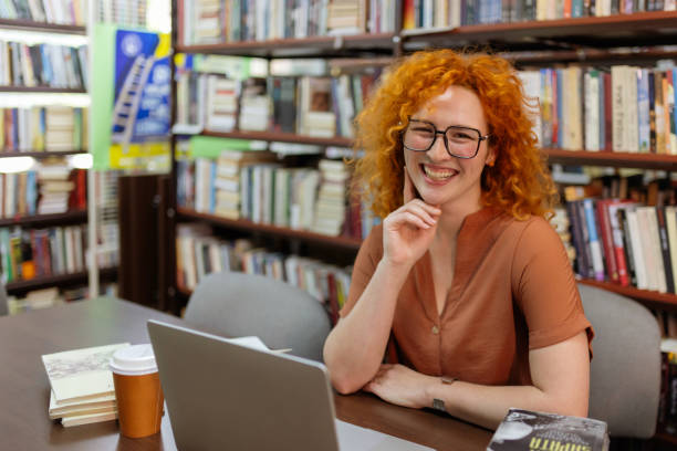 istock Redhead with Curly Hair and Glasses Smiling at Camera in Library 2190441468