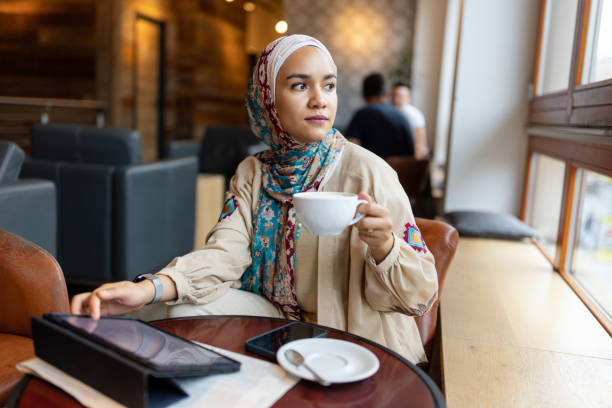 istock Woman in Hijab Looking Out Window with Coffee 2190441939