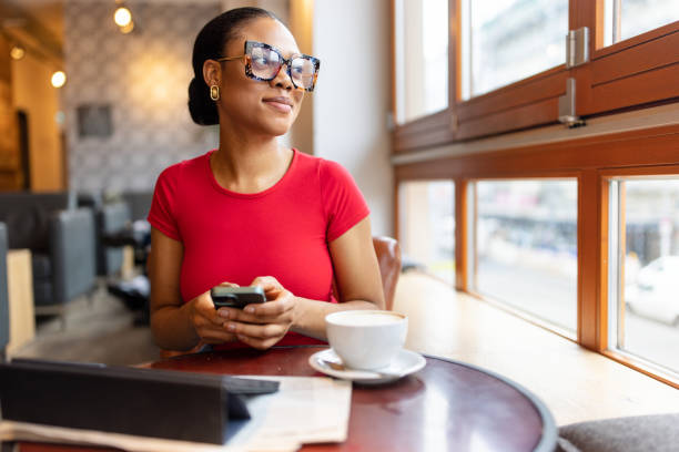 Confident woman gazing out the window while holding a smartphone in a modern cafe.