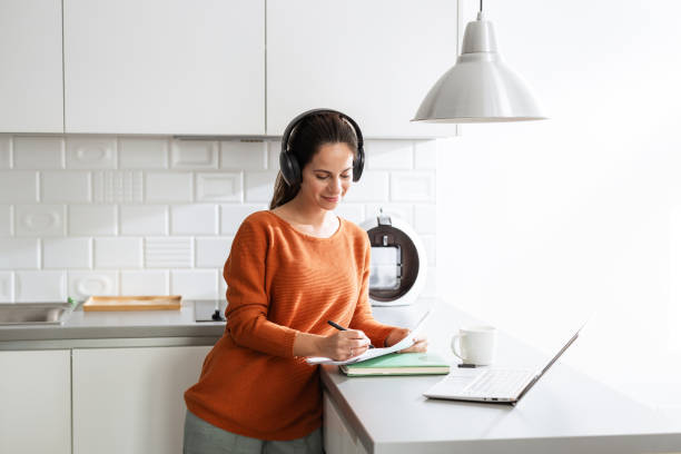 istock Woman working at home using headphones and a laptop in a modern kitchen 2190444025