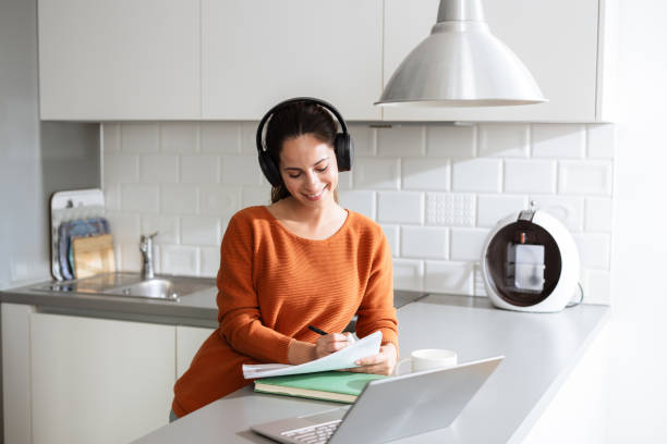 istock Woman writing notes while listening to an online class in a modern kitchen 2190444032