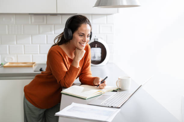 istock Young woman with headphones, taking notes while listening to online class 2190444038