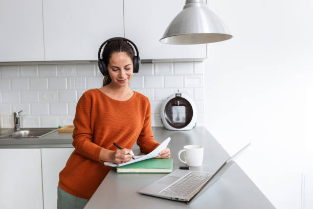 istock Young woman with headphones working from home in a modern kitchen setting 2190444044
