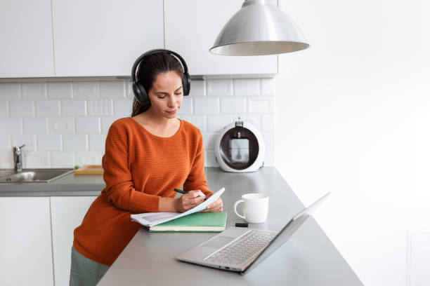 istock Young woman with headphones working from home in a modern kitchen setting 2190444049