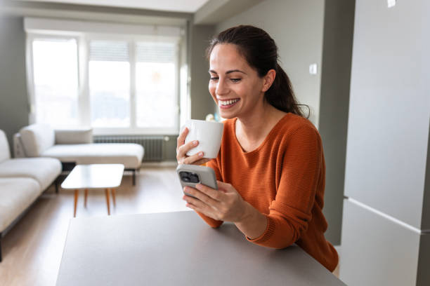 Smiling woman using smart phone while enjoying coffee in a cozy home setting