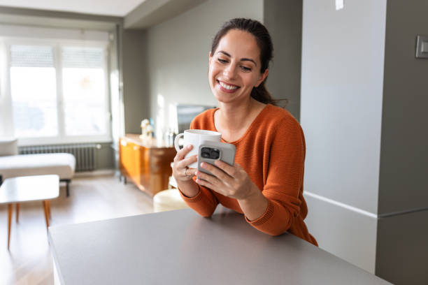 istock Smiling woman using smart phone while enjoying coffee in a cozy home setting 2190444072