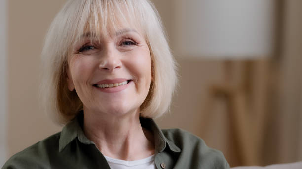 istock Front view portrait mature blonde smiling caucasian woman looking at camera posing in studio portrait, cheerful older grey-haired female granny in white t-shirt, healthy carefree senior retired lady 2190446568