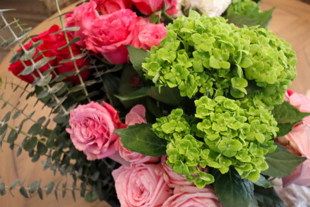 istock A vibrant bouquet featuring bright green hydrangeas, pink and red roses, eucalyptus stems, and white hydrangeas, artfully arranged with lush greenery on a wooden table. 2190450227