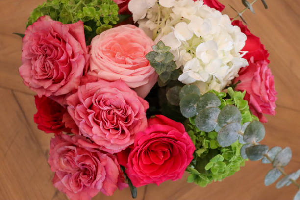 istock A beautifully arranged bouquet showcasing pink and red roses, white hydrangeas, green hydrangeas, and eucalyptus leaves, offering a vibrant mix of colors and textures on a wooden surface. 2190450999