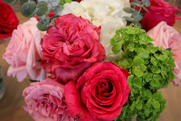 istock A vibrant bouquet featuring red and pink roses, white hydrangeas, green hydrangeas, and eucalyptus leaves, arranged in soft textures and rich colors, displayed elegantly on a wooden surface. 2190451271