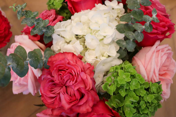 istock A captivating bouquet featuring vibrant pink and red roses, white hydrangeas, green hydrangeas, and eucalyptus leaves, elegantly arranged with soft textures and bold colors on a wooden surface. 2190451295
