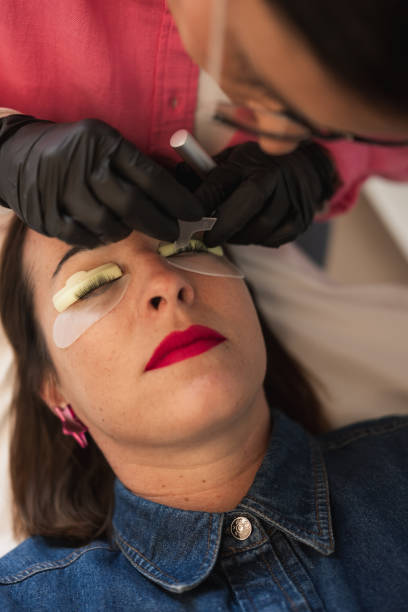 Beautician is using a tool to apply an eyelash lift treatment to a customer in a beauty salon