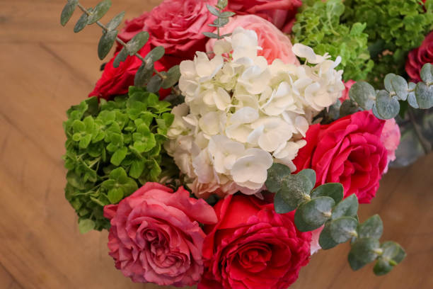 istock A vibrant arrangement featuring pink and red roses, lush green hydrangeas, white hydrangeas, and eucalyptus, elegantly displayed on a wooden surface for a fresh and romantic touch. 2190453591