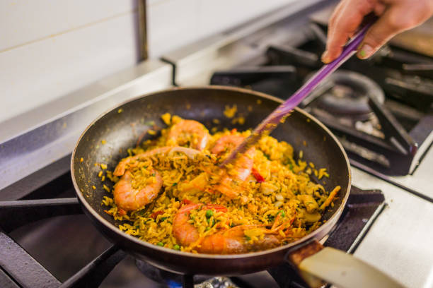 Chef using spatula to stir rice and shrimp dish in frying pan on stovetop in a commercial kitchen, preparing traditional ecuadorian food in Portoviejo, ecuador