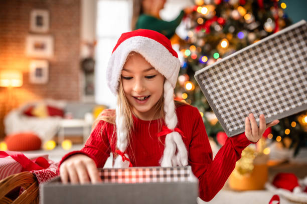 istock Joyful girl opening Christmas gift by a beautifully lit tree at home 2190457561