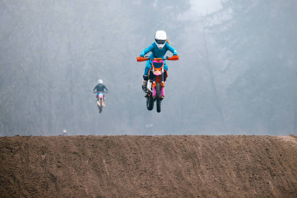 A Caucasian teenager partakes in women's motocross racing, speeding through laps on a track with jumps and berms.  Shot in Washington state, USA.