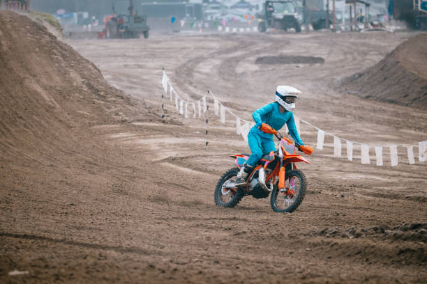 A Caucasian teenager partakes in women's motocross racing, speeding through laps on a track with jumps and berms.  Shot in Washington state, USA.