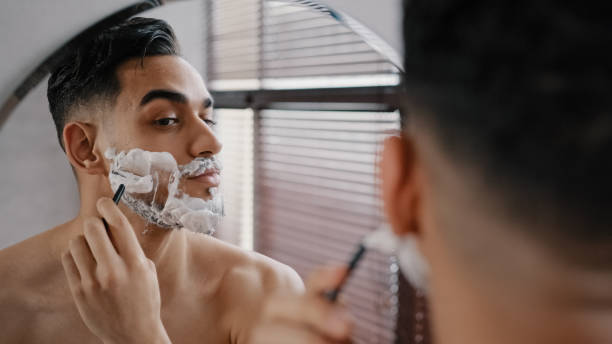 istock Hispanic arabian arab indian bearded handsome man shaving using disposable razor in bathroom looking at mirror. Daily morning routine male hygienic beauty procedure. Guy shaves beard and moustache 2190466756
