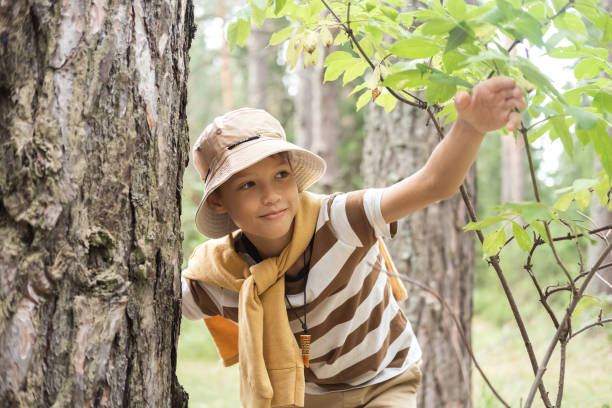 istock A little boy on a walk in the forest or park, peeking out from behind a tree. 2190480589
