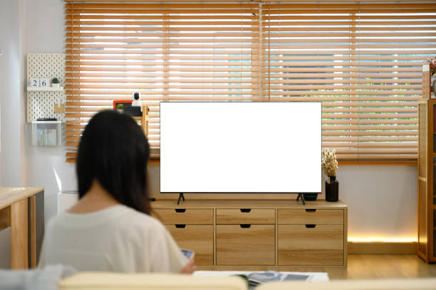 istock Back view of woman holding a remote control watching a large blank television screen 2190487309