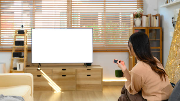 istock Back view of woman holding a remote control watching a large blank television screen 2190487407