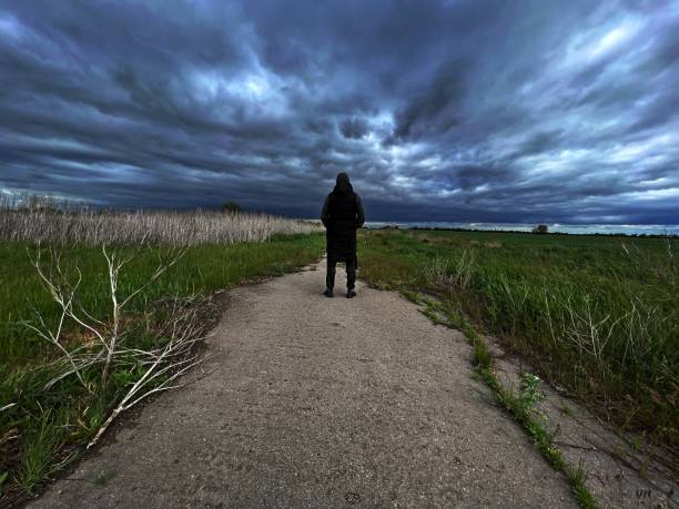 istock Man in dark coat standing in field against gloomy sky rear view. 2190489977