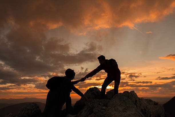 Hiking team helping each other friend giving a helping hand while climbing up on the mountain rock adventure travel concept of friendship support trust teamwork success. Couple hiking at sunset. High quality photo