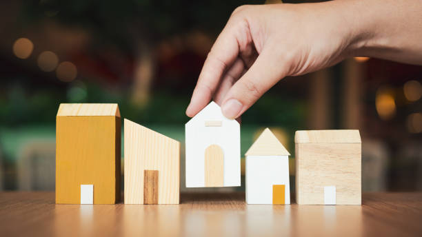 istock Hand choosing mini wood house model from model on wood table, selective focus, Planning to buy property. Choose what's the best. A symbol for construction ,ecology, loan concepts 2190491813
