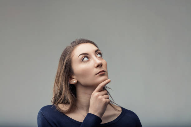 istock Young woman thinking and looking up with hand on chin 2190492025