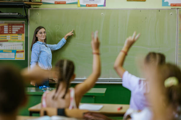 istock Teacher engaging with students by writing on a green chalkboard in a classroom during a lesson in the afternoon 2190497592