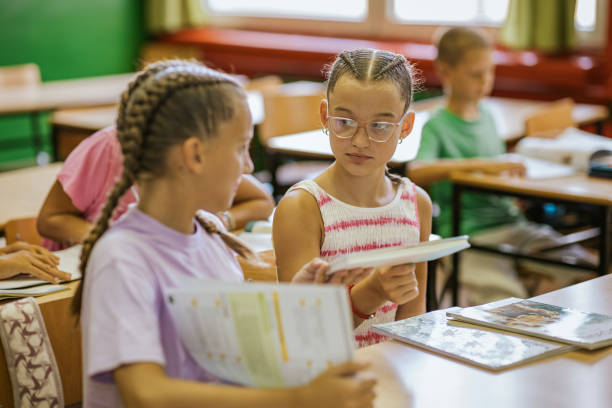 istock Students enjoy a lively break between lessons, interacting and sharing books in a bright classroom setting 2190497718