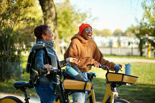 Three-quarter front view of female friends in 20s and 30s wearing warm casual clothing, resting from riding, talking and laughing.