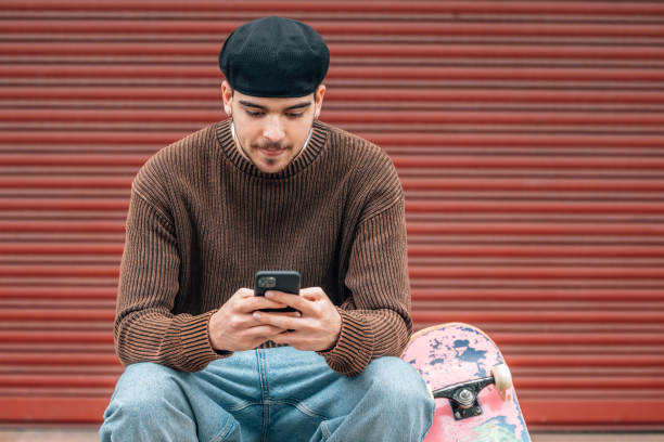 istock young man on the street with mobile phone and skateboard 2190502993