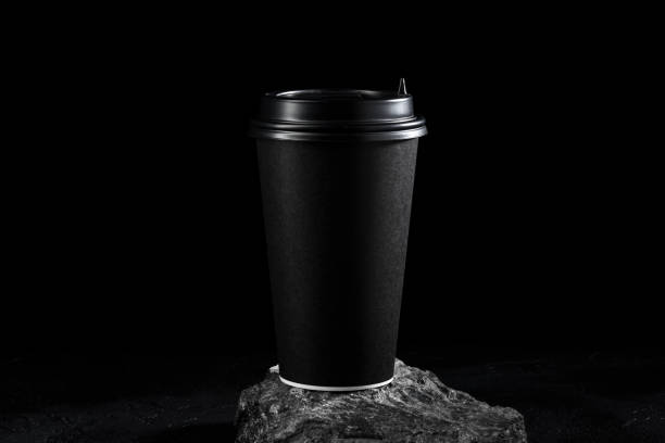 istock Black coffee cup stands on a textured rock surface against a dark background 2190505809