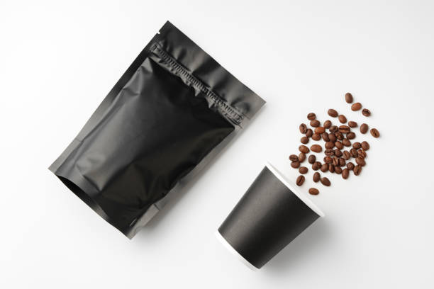 istock Freshly roasted coffee beans beside a takeout cup and black packaging on a white surface 2190506652