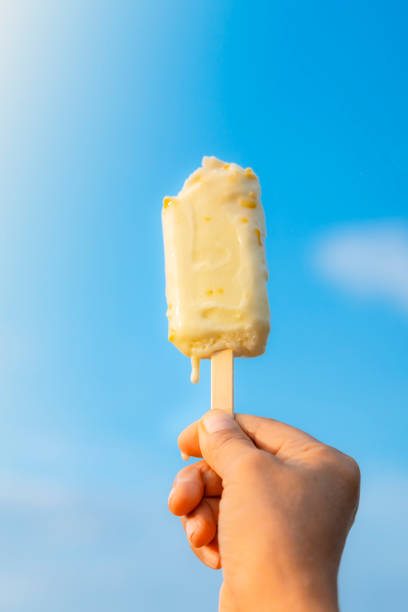 istock A woman's hand holding a corn ice cream raised to the blue sky in summer. 2190507936