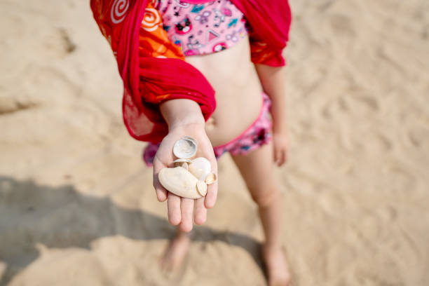 A joyful child eagerly displays an array of colorful seashells while delighting in a beautiful sunny day at the beach