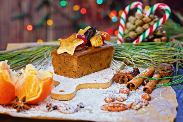Christmas fruit cake garnished with marzipan star, dried fruits, and nuts, surrounded by spices, oranges, and pine branches on rustic table