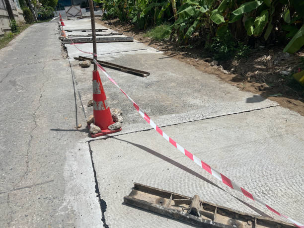 istock Damaged concrete road section marked with safety cone and red-white warning tape, showing cracks and exposed infrastructure requiring repair 2190510583
