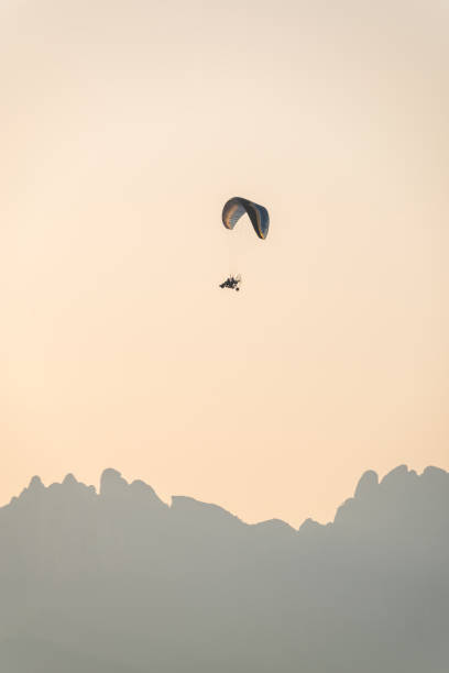 Powered paraglider gliding across rugged montserrat peaks, silhouetted against warm sunset hues, capturing aerial freedom and mountainous landscape beauty
