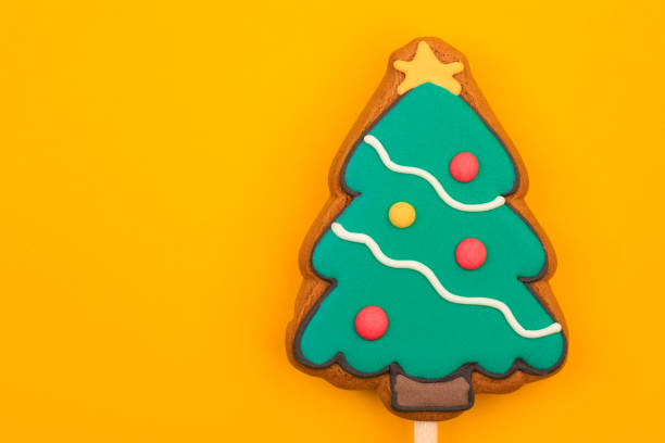 Festive Christmas Tree shaped gingerbread cookie pop with colorful icing on yellow background