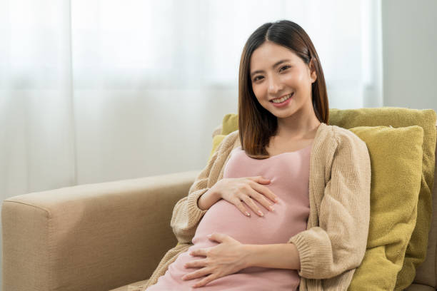 Happy pregnant woman caresses her belly while taking rest on sofa at home, concept of happy motherhood waiting for childbirth, family planning and pregnancy with insurance for child health. stock photo