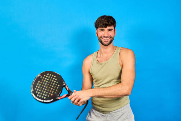 istock Young sportsman smiling and holding paddle racket on blue background 2190518861