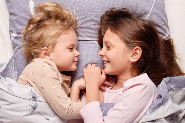 istock Two young sisters are lying closely in bed, engaged in a joyful conversation. Their expressions are filled with happiness as they share a heartwarming connection in their cozy room 2190522071