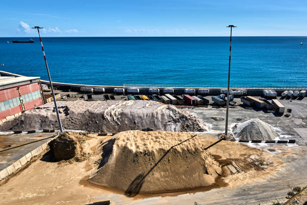 Savona. Italia - December 18, 2024: Coastal industrial area with sand piles, shipping containers and a clear blue sea in Savona, Italy. Concept: Juxtaposition of industrial elements and natural beauty