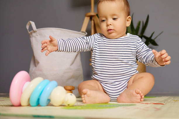 istock A young child sits on a soft mat surrounded by vibrant stacking toys and a bag, curiously reaching for the colorful rings. The warm indoor light creates a playful atmosphere 2190524896