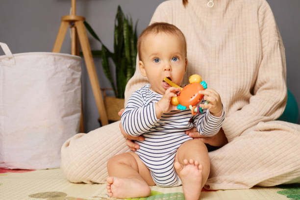 istock A young child sits on a soft mat, focused on a vibrant toy. The room features modern decor, with plants in the background, creating a warm atmosphere for playtime 2190524925